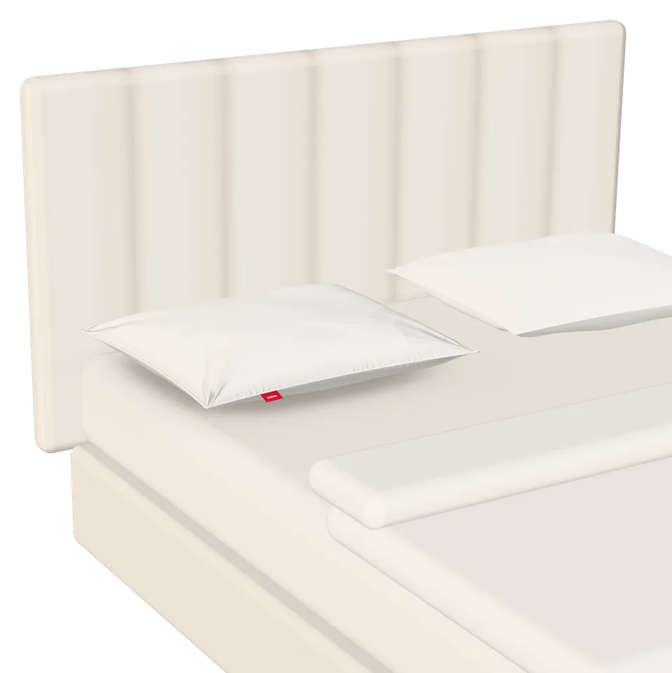 Het kussen ligt uitgepakt en volledig opgebold in een opgemaakt bed.