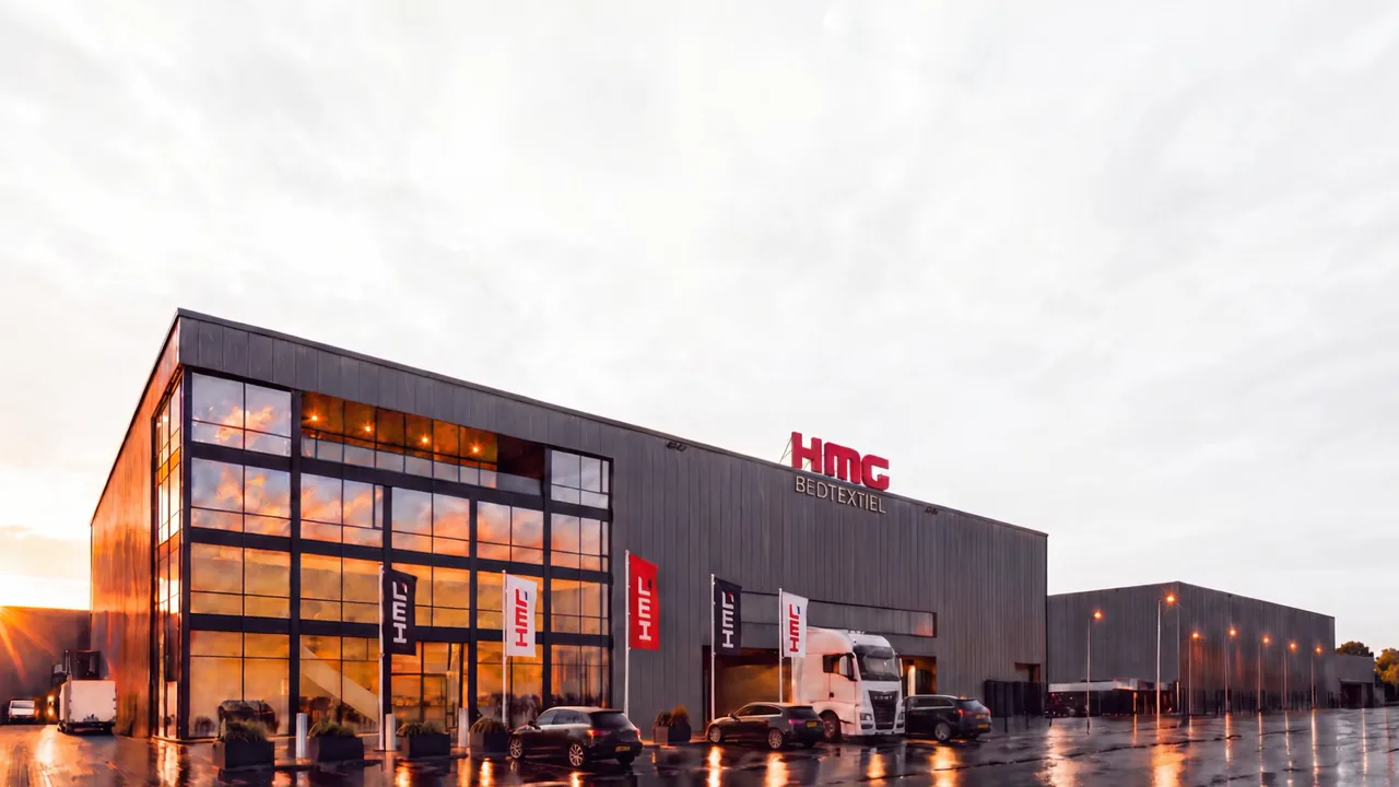De glazen gevel van de fabriek van HMG Bedtextiel in Eindhoven, in het avondlicht